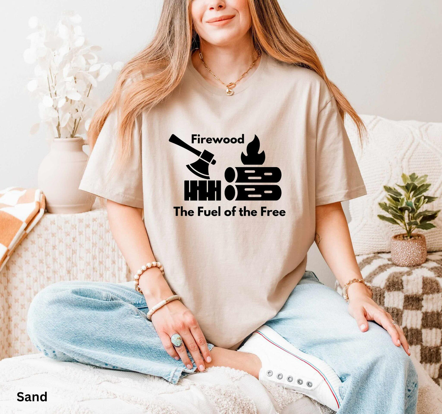 Sand Colored T-shirt with the phrase 'Firewood: The Fuel of the Free,' featuring a campfire, stacked firewood, and an ax—perfect for wood heat lovers and homesteaders.