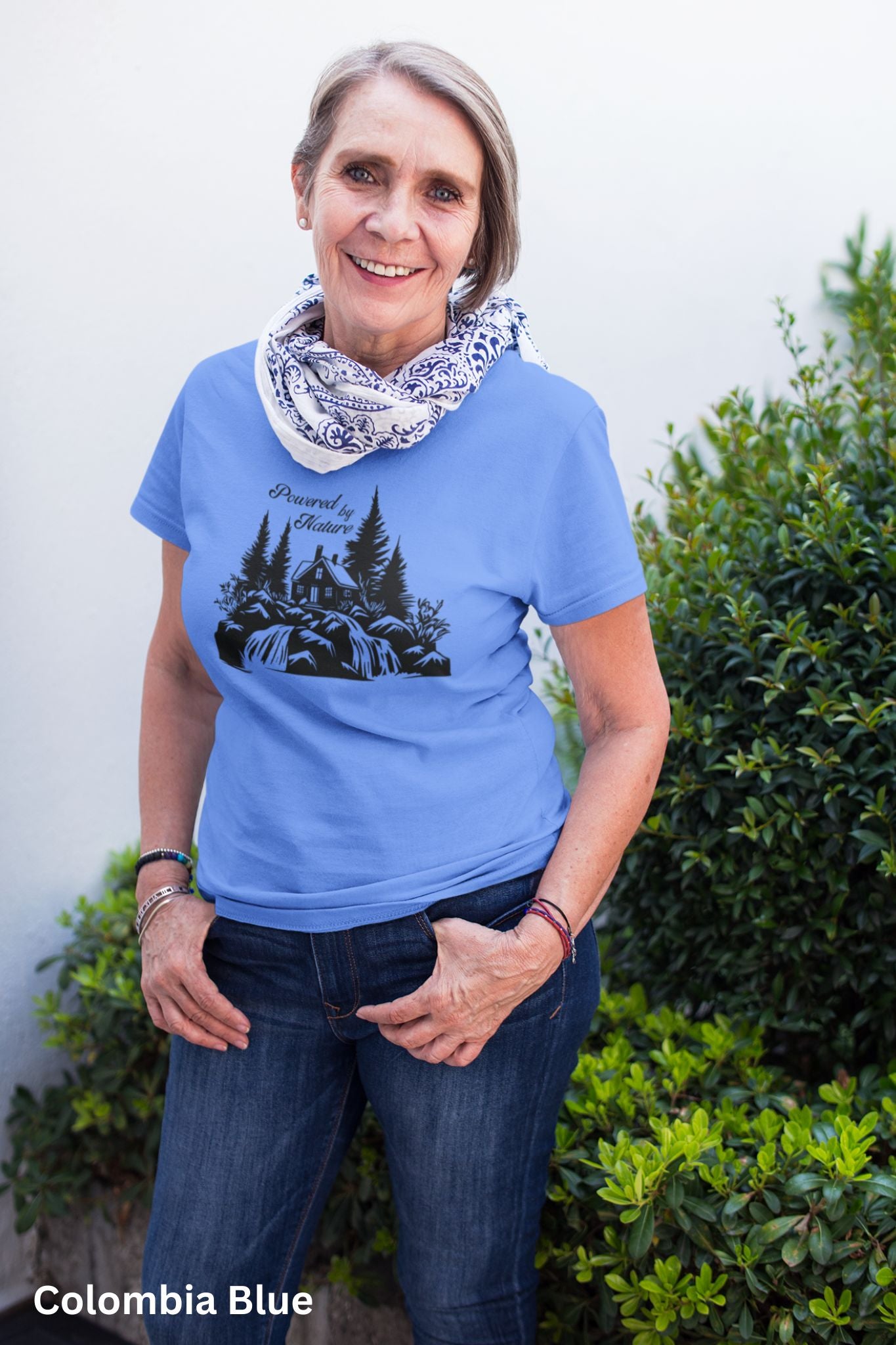 Blue T-shirt with the phrase 'Powered by Nature,' featuring a detailed cabin in the woods, a cascading waterfall, and trees—perfect for outdoor and adventure lovers