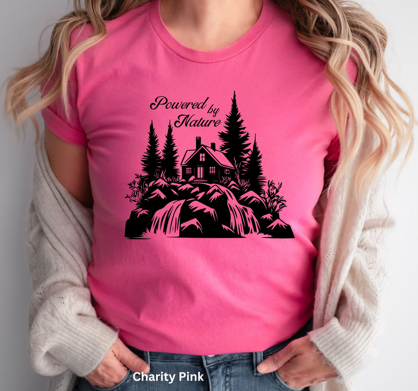 Pink T-shirt with the phrase 'Powered by Nature,' featuring a detailed cabin in the woods, a cascading waterfall, and trees—perfect for outdoor and adventure lovers