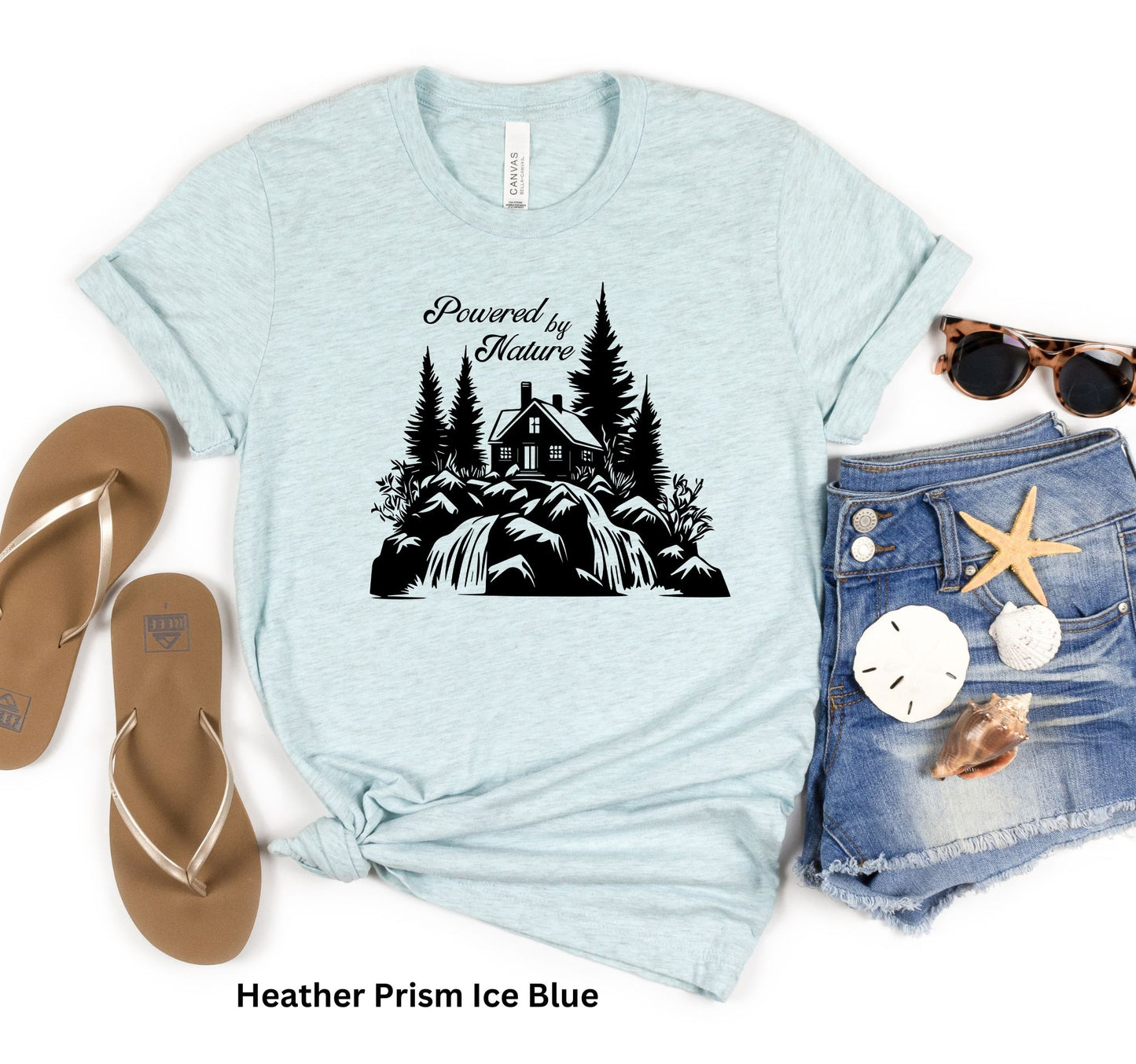 Light Ice Blue T-shirt with the phrase 'Powered by Nature,' featuring a detailed cabin in the woods, a cascading waterfall, and trees—perfect for outdoor and adventure lovers