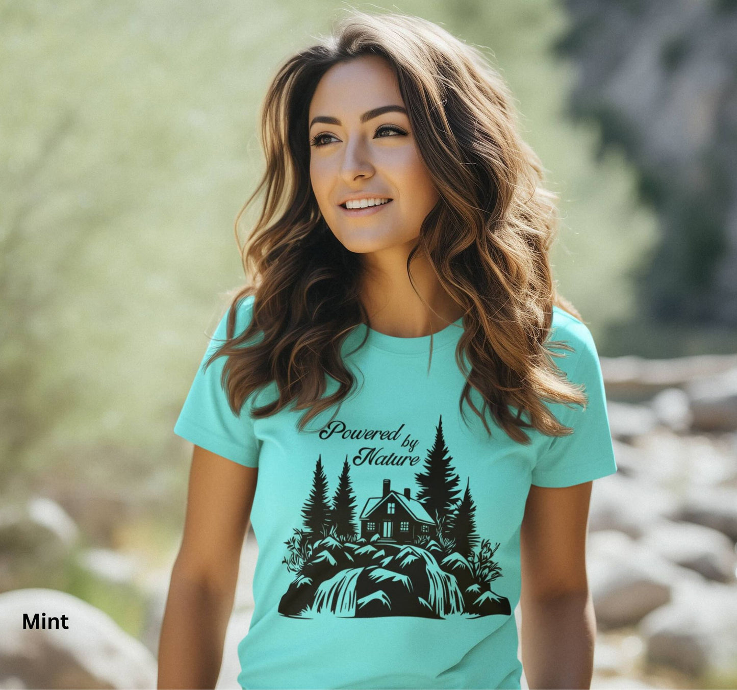 T-shirt in mint color with the phrase 'Powered by Nature,' featuring a detailed cabin in the woods, a cascading waterfall, and trees—perfect for outdoor and adventure lovers