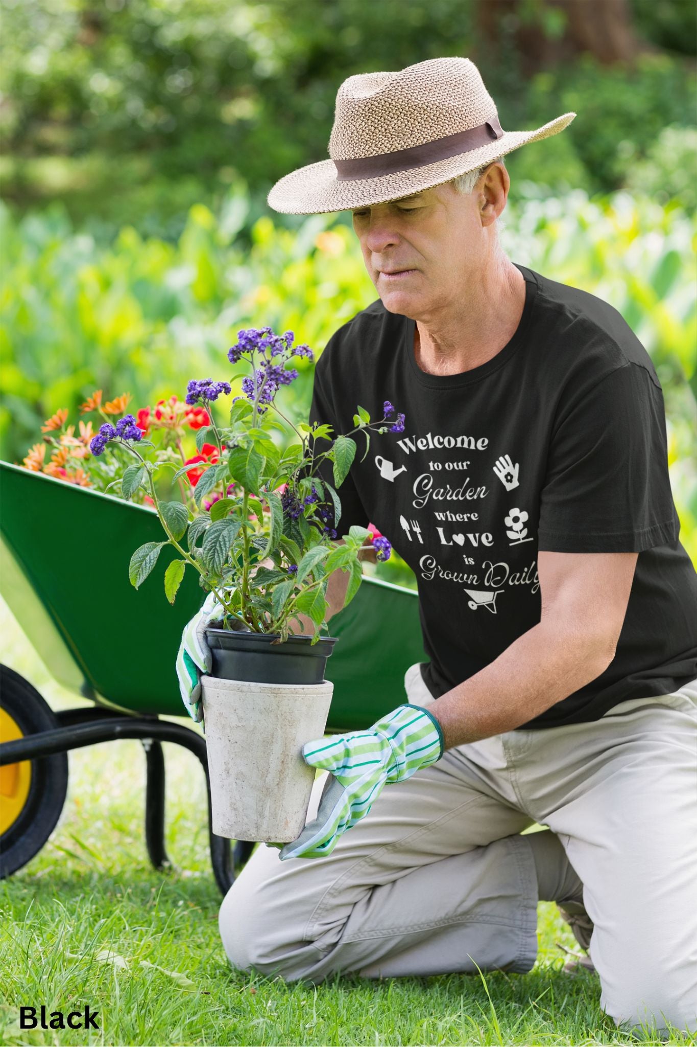 Black T-shirt with the phrase 'Welcome to our Garden where love is grown daily,' featuring gardening tools, a heart, a wheelbarrow, a flower, gloves, and a watering jug.
