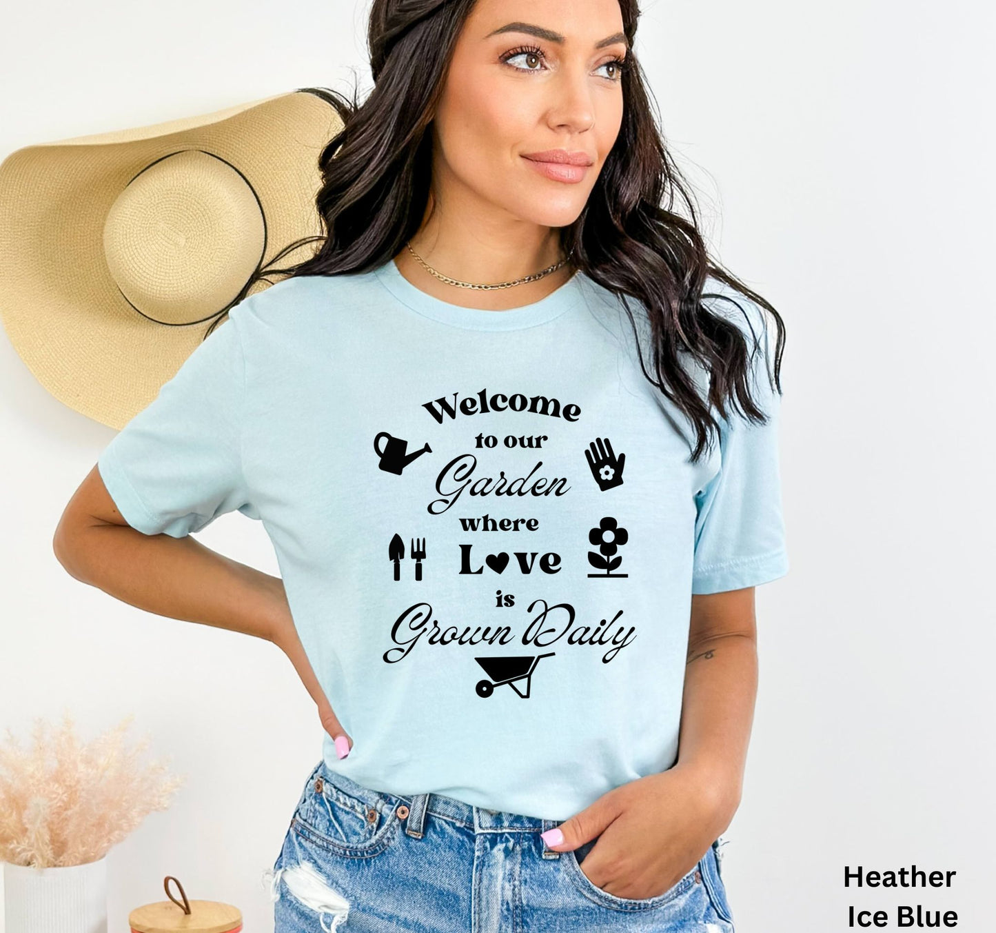 Light Blue T-shirt with the phrase 'Welcome to our Garden where love is grown daily,' featuring gardening tools, a heart, a wheelbarrow, a flower, gloves, and a watering jug.