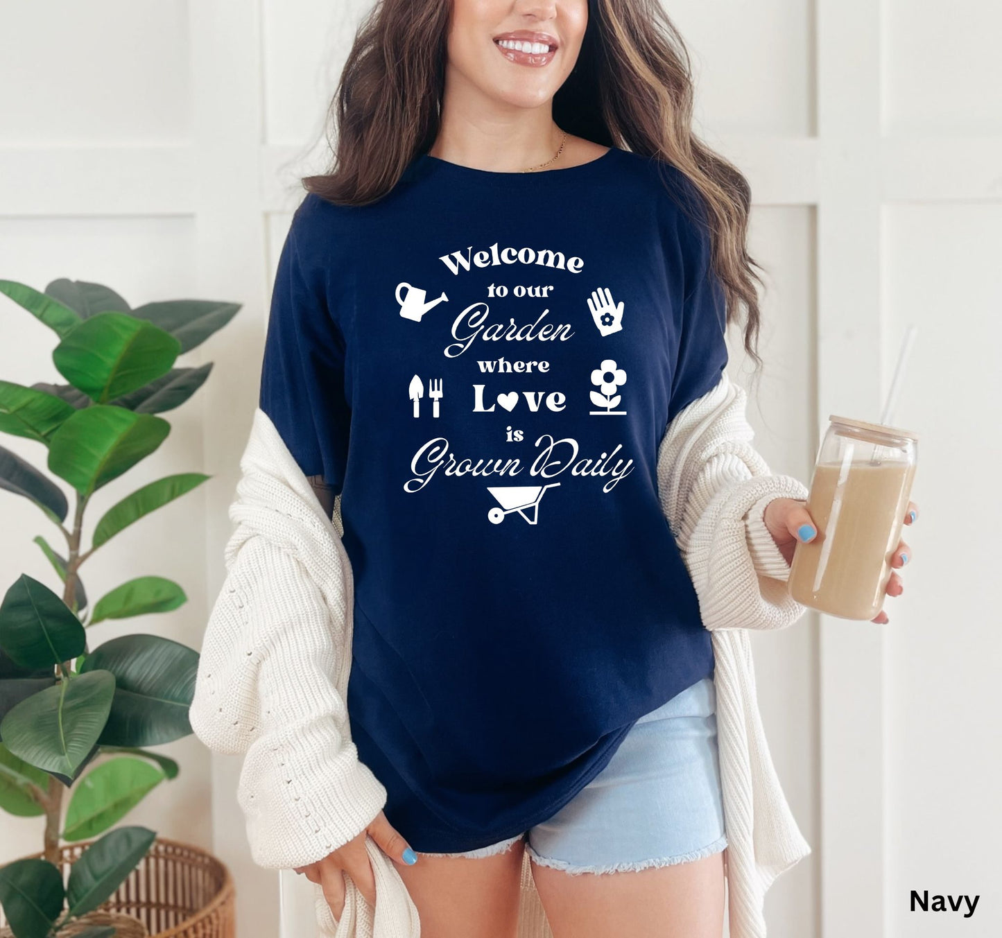 Navy T-shirt with the phrase 'Welcome to our Garden where love is grown daily,' featuring gardening tools, a heart, a wheelbarrow, a flower, gloves, and a watering jug.